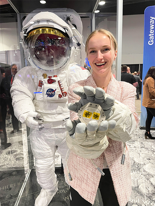 Person holding RAFTI with astronaut gloves and astronaut spacesuit in background