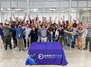 Cleanroom grand opening photo. Team stands with hands outstretched in front of the cleanroom.