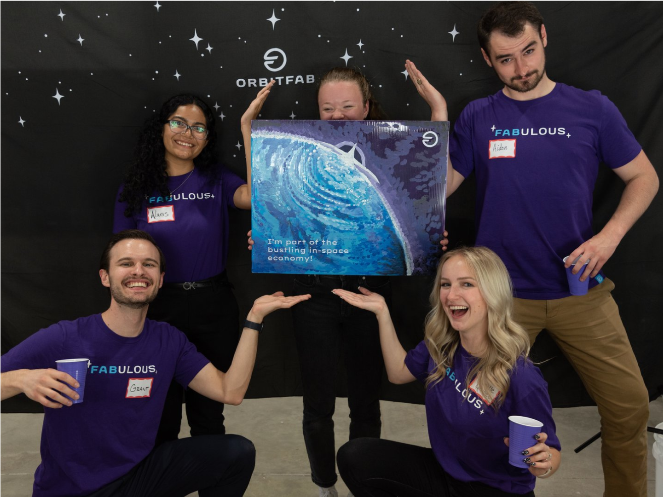 Five people in purple shirts holding a painting of Earth