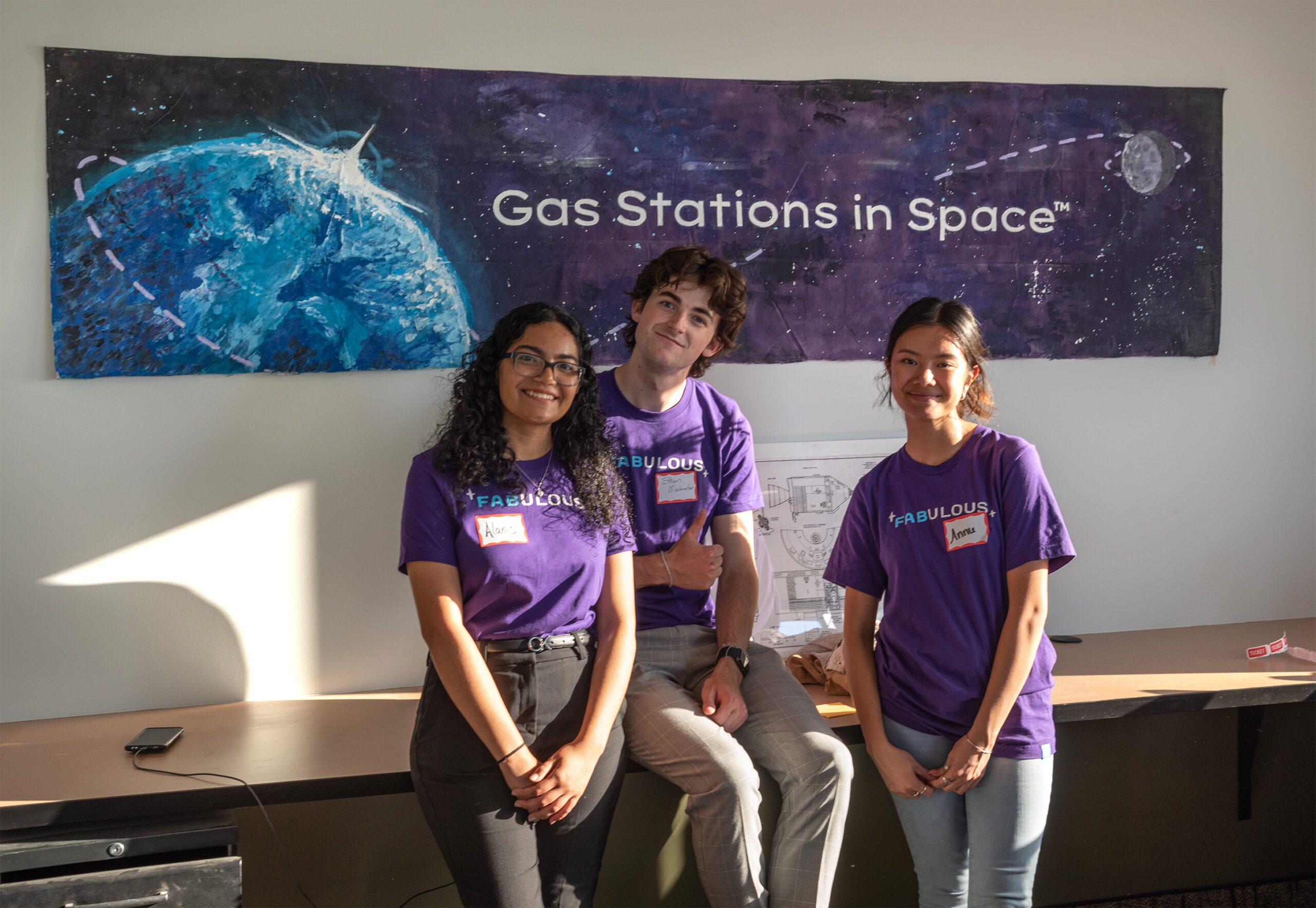 Three interns in front of Gas Stations In Space painted mural